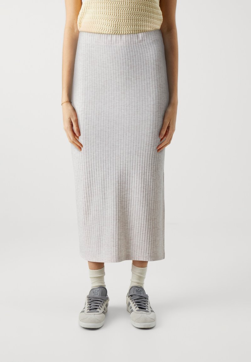 Maxi-Rock aus grauem Rippstoff, mit einem engen Taillenbund, kombiniert mit grauen Turnschuhen und cremigen Socken. Glatte Textur.