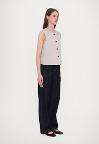 Haut sans manches gris clair avec des rayures verticales et cinq boutons noirs, assorti à un pantalon large en denim noir avec des coutures vertes.