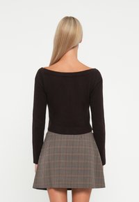 Sort croppet genser med avskåret design og lange ermer, paret med et rutete skjørt i beige, brune og svarte farger.