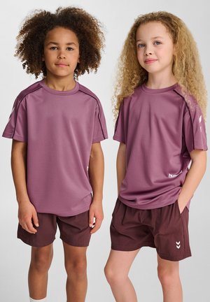 Dwoje dzieci noszących dopasowane purpurowe koszulki sportowe i brązowe szorty. Koszulki mają krótkie rękawy i oddychający materiał; szorty są luźne.