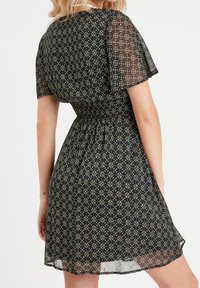 Robe noire à fleurs avec des manches courtes transparentes, une taille smockée et un tissu léger. Présente un petit motif géométrique en vert et rouge.