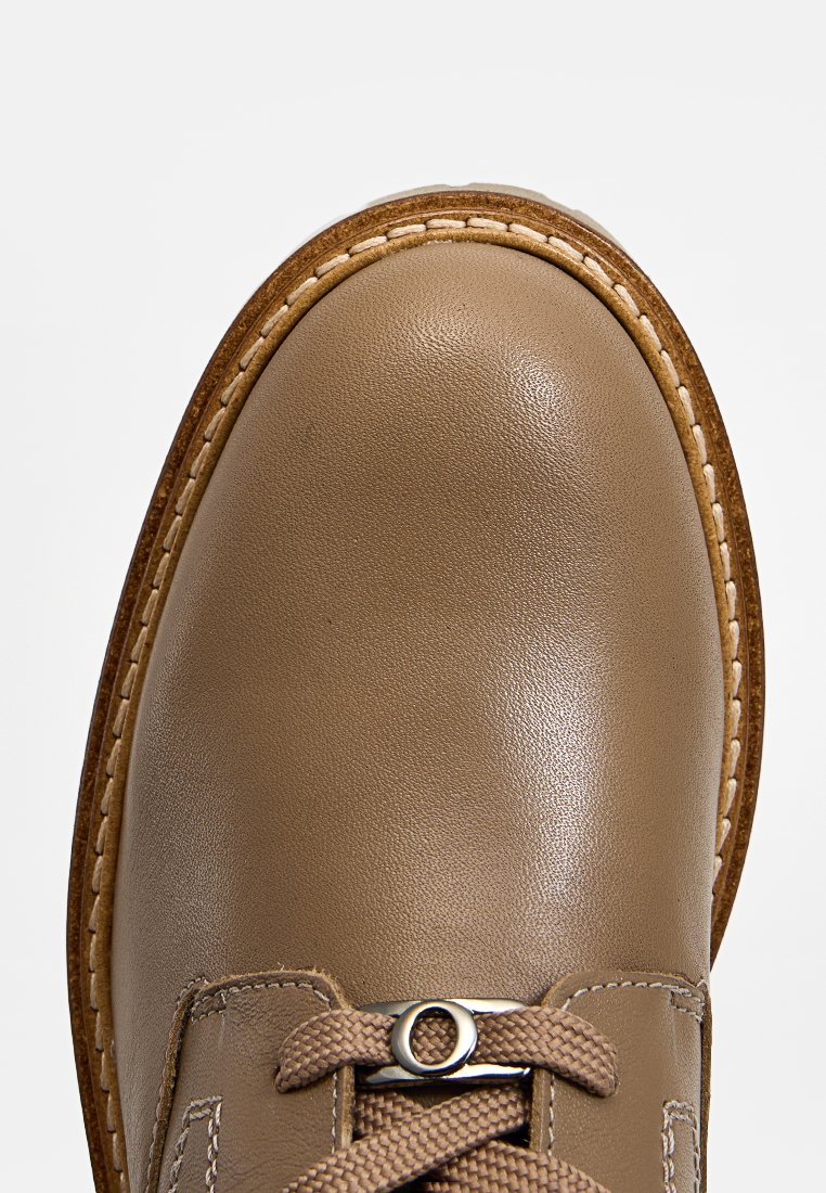 Chaussure en cuir brun avec un bout arrondi, comportant des détails cousus et un laçage. La tige a une texture lisse et une semelle beige.