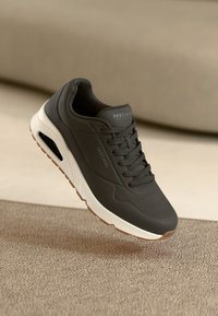 Czarne buty sportowe z teksturowaną cholewką, sznurowanym designem, białą podeszwą środkową i brązową gumową podeszwą. Posiadają detal w postaci bocznego wentylu.