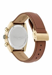 Zlaté hodinky so puzdrom z nehrdzavejúcej ocele a hnedým koženým remienkom. Majú jednoduchý oválny tvar, štruktúrovaný remienok a vyrytý logo na zadnej strane.