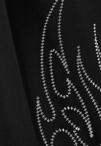 Μαύρο ύφασμα με περίπλοκα ασημένια κεντημένα σχέδια φλόγας. Ο σχεδιασμός περιλαμβάνει ζιγκ-ζαγκ ραφές για υφή και λεπτομέρεια.