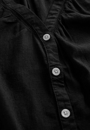 Must mustrained shirt, mille de jae peal ja nuppudega esipaneel. Omab valgeid nuppe ja rynkselg, näidates tekstuurset pinda.
