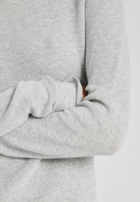 Világosszürke kötött pulóver bordázott textúrával és hosszú ujjakkal, lazább fazonnal, enyhén felgöngyölített mandzsettákkal.