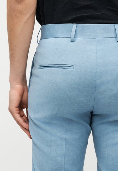 Κοντινή λήψη ενός ατόμου που φοράει ανοιχτό γαλάζιο παντελόνι με ρεβέρ και πίσω τσέπες με σχισμές, καθώς και θηλιές για ζώνη, συνδυασμένο με μαύρο πουκάμισο.