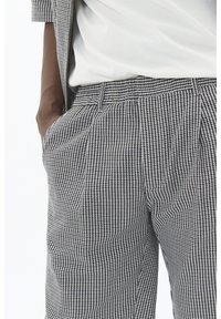 Pantaloni în carouri alb-negru, dintr-un material texturat, cu buzunare laterale și o croială lejeră, asortați cu un top alb.