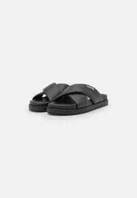 Svarta sandaler med slät syntetisk yta, korsande remmar och en strukturerad sula. Har en liten logotyp på remmen.