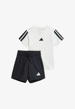 Camiseta blanca con el logo negro de Adidas y tres rayas negras en las mangas, combinada con pantalones cortos negros que tienen una cintura elástica y un logo.