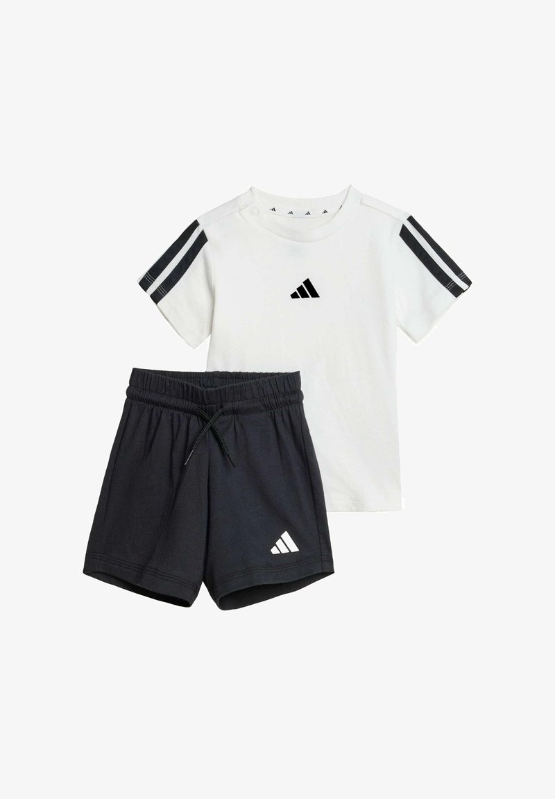 Biele tričko s čiernym logom Adidas a tromi čiernymi pruhmi na rukávoch, doplnené čiernymi šortkami s elastickým pásom a logom.