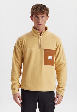 Pullover in pile giallo con collare a mezza zip, tasca sul petto marrone e tasca laterale con zip. Texture confortevole e vestibilità rilassata.