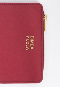 Cartera Bimba y Lola en tejido burdeos, con cierre de cremallera y acento de logo dorado. Textura suave con detalles de doble costura.