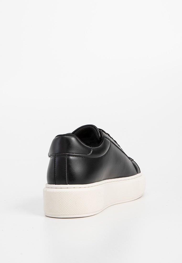 Zapatilla de cuero negro con punta redonda, textura suave y suela de goma blanca. Presenta un diseño minimalista y detalles de cordones.