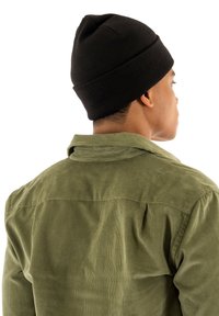 Chemise en velours côtelé vert avec un empiècement dans le dos et un bonnet en tricot noir, vue de dos. Les matériaux ont une finition texturée.