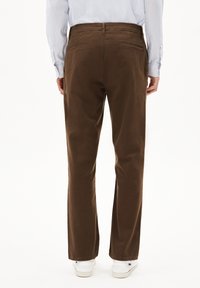 Pantalon en coton marron à coupe droite, avec deux poches arrière et des ourlets retournés, associé à des baskets blanches.