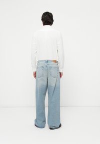 Light blue denim wide-leg jeans with a faded finish, featuring back pockets and a leather label on the waistband, paired with a white shirt.
