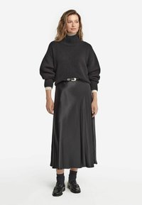 Svart stickad tröja med hög polokrage och puffärmar, tillsammans med en slank, svart, satin A-linjeformad kjol och glänsande svarta loafers.