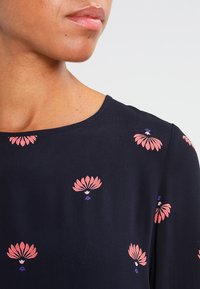 Marinblus med rund halsringning, prydd med blommönster i rosa och lila. Mjukt tyg med en slät textur; korta ärmar synliga.