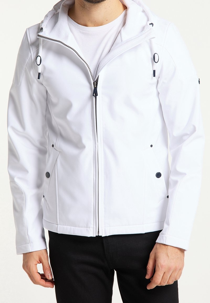 Mężczyzna ubrany w biały polar z kapturem na zamek i ściągaczami, na białej koszulce i czarnych spodniach, stojący na jednolitym tle.