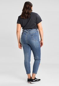 Džínové kalhoty s vysokým pasem, modré barvy, se sníženým siluetou, s zadními kapsami a odřením na levém stehně. V kombinaci s černým tričkem.