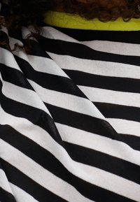 Gestreifter Stoff in Schwarz und Weiß mit einer strukturierten Oberfläche und einem neongrünen Kragen. Die Streifen variieren in der Breite und bilden ein markantes Muster.
