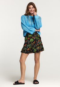 Maglione lavorato a maglia di un blu chiaro con motivo a trama aperta, abbinato a una gonna nera con volant caratterizzata da colorati disegni di palme. Sandali neri piatti.