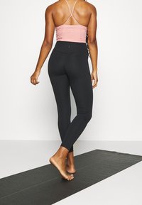 Czarne legginsy z wysokim stanem połączone z różowym topem na ramiączkach. Legginsy mają gładką fakturę i dopasowany krój.