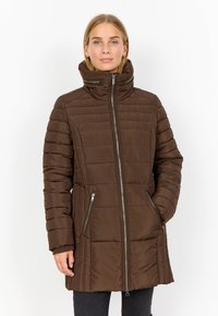 Brun pufferjacka med hög krage, dragkedja framtill och sidofickor. Tyget har ett vadderat mönster med en mjuk textur.