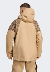 Bež vodootporna jakna s uzorkom u smešnom tonu, podesivim kapuljačom i detaljem logotipa na rukavu. Glatka tekstura i praktičan dizajn.
