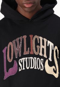 Schwarzer Hoodie mit mehrfarbigen, strukturierten Stickbuchstaben "LOWLIGHTS STUDIOS" im Patchwork-Design.