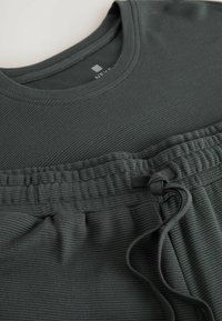 Tamnozeleni rebrasti materijal majice s okruglim izrezom, u kombinaciji s hlačama jogger stila koje imaju elastičnu ušicu i detalj sa vezicom.