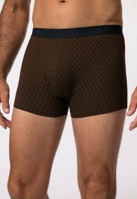 Boxer shorts marron avec un motif géométrique, dotés d'une ceinture sombre étiquetée "JP1880." Fabriqués en un matériau lisse et extensible.