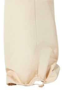 Beige szövetnadrág, behúzott szegéllyel, sima textúrával és finom fényességgel. Állítható méretű húzózsinórral rendelkezik.