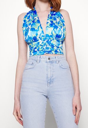 Niebiesko-zielony kwiatowy krótki top na szyję ze zmarszczonym przodem, noszony z jasnoniebieskimi, wysokim stanem jeansami na osobie z rudymi włosami.