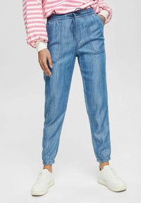 Ljust blå denim-joggingbyxor med elastiskt midjeband och dragsko. Avsmalnande ben med samlade muddar och framfickor. Bärs med vita sneakers.