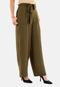 Pantaloni a gamba larga verde oliva con tessuto testurizzato, vita cinchata e dettaglio con fiocco. Abbinati a scarpe con tacco nere.