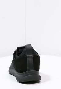 Zapatillas negras con parte superior de ante y acentos de cuero, que cuentan con una suela de goma gruesa y una pestaña en la parte posterior para facilitar su puesta.