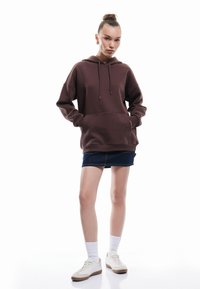 Bruine hooded sweatshirt met trekkoorden, kangoeroezak, relaxte pasvorm, gecombineerd met een denimrok en witte sneakers. Glad textuur.