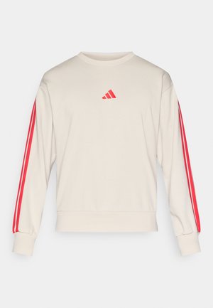 Beige Langarm-Sweatshirt mit rotem Adidas-Logo auf der Brust und drei roten Streifen, die entlang jedes Ärmels verlaufen.