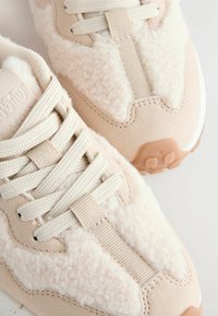 Baskets de sport beiges en suède et textile doux, à bout rond, avec des lacets épais et une semelle extérieure en caoutchouc texturé offrant une bonne adhérence.