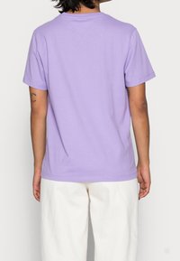 T-shirt in cotone viola con maniche corte e vestibilità rilassata. La vista posteriore mostra un design semplice e un colletto a girocollo. Nessuna grafica o pattern.