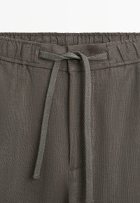 Ceinture élastique gris foncé avec cordon en tissu noué en un nœud sur un pantalon en lin ou coton texturé.