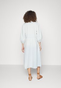 Vestito celeste, lungo fino al ginocchio, realizzato in un tessuto morbido, caratterizzato da maniche a sbuffo, una vita definita e una vestibilità rilassata. Accentato da una texture liscia.