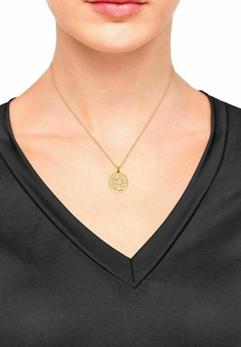 Donna che indossa una maglietta nera a V e una collana dorata con un ciondolo rotondo e traforato che poggia sul suo petto superiore.
