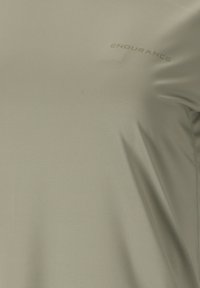 Tessuto verde chiaro con una trama, con la parola "ENDURANCE" stampata in lettere piccole e discrete vicino alla parte superiore del torace.