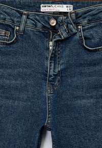 Jeans de mezclilla en azul oscuro con un ajuste slim y acampanado. Diseño de cintura alta, detalles de costura en naranja, botón de metal y cierre de cremallera. Talla W27 L32.