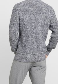 Gestrickter Pullover in dunkelblauen und hellgrauen Farbtönen mit geripptem Muster, Rundhalsausschnitt und eng anliegenden Bündchen, kombiniert mit grauen Sweatpants.