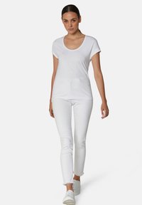 Witte korte mouwen t-shirt met een ronde hals, gecombineerd met witte denim jeans. De jeans hebben een rafelige zoom en worden gedragen met witte sneakers.